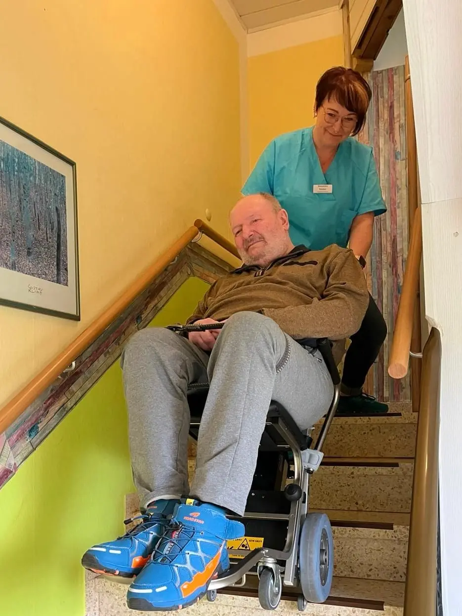 Eine Pflegefachkraft begleitet einen Klienten im Treppensteiger sicher die Treppe hinunter