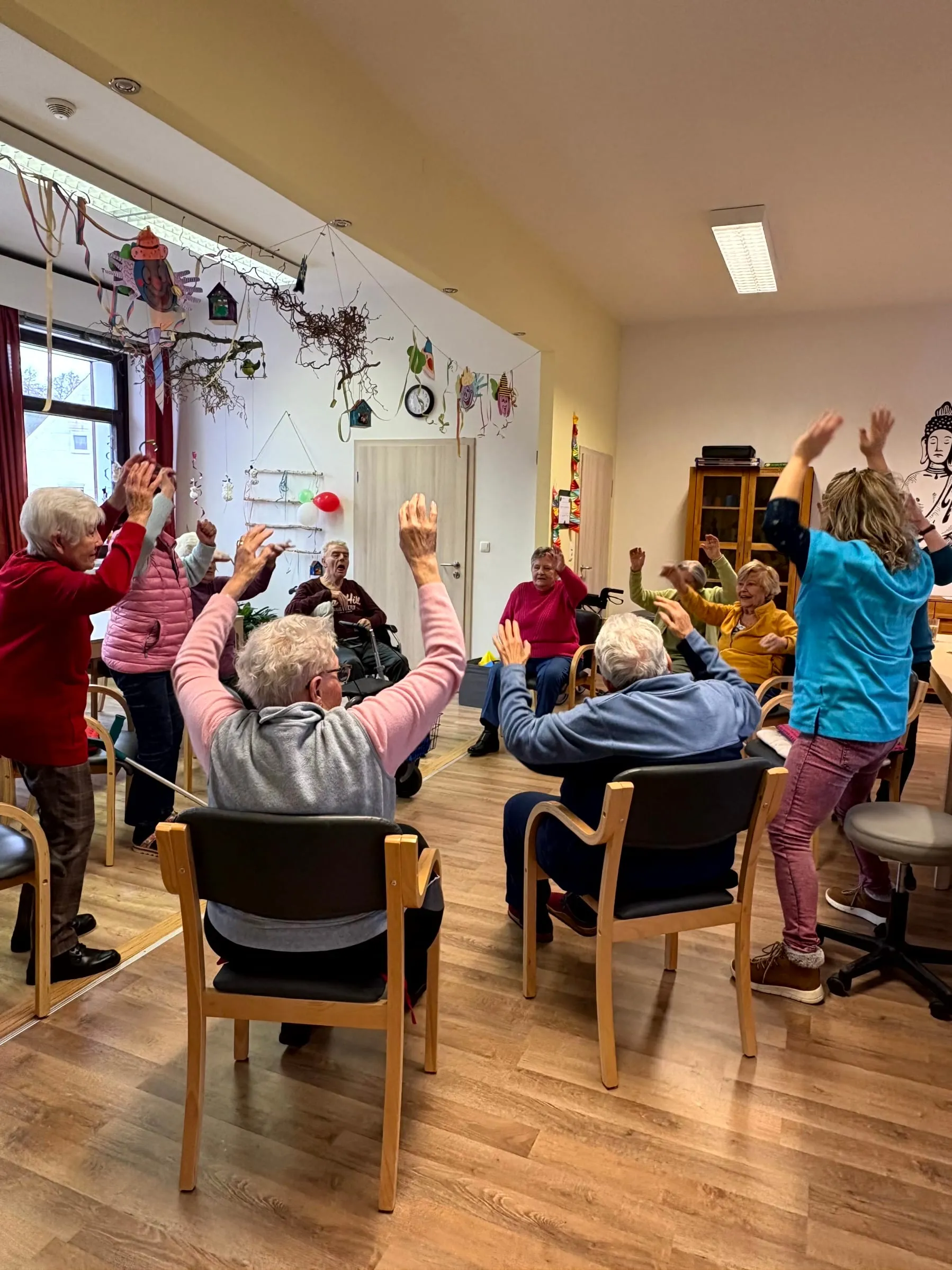 Gruppe hebt gemeinsam die Arme bei der Sitzgymnastik