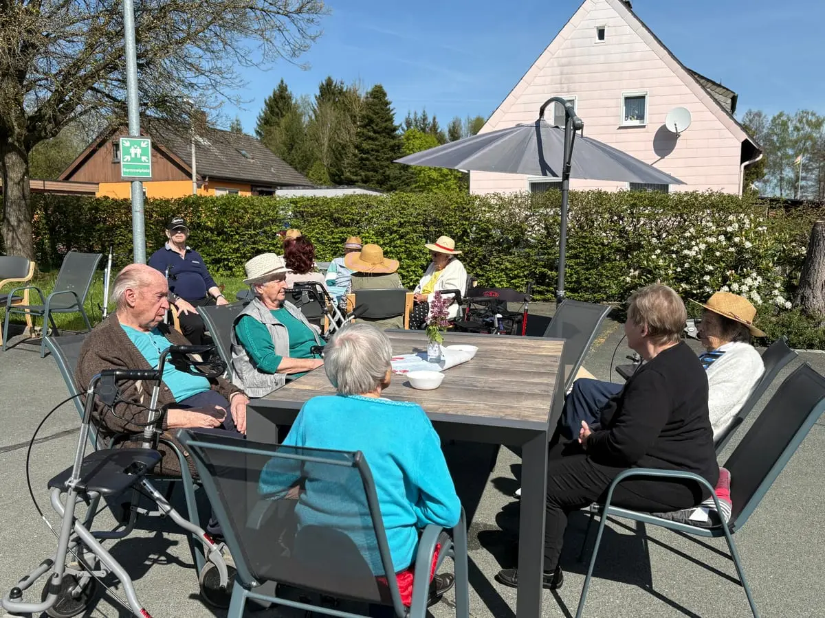 Gäste sitzen bei Sonnenschein unter dem Sonnenschirm im Freien beisammen
