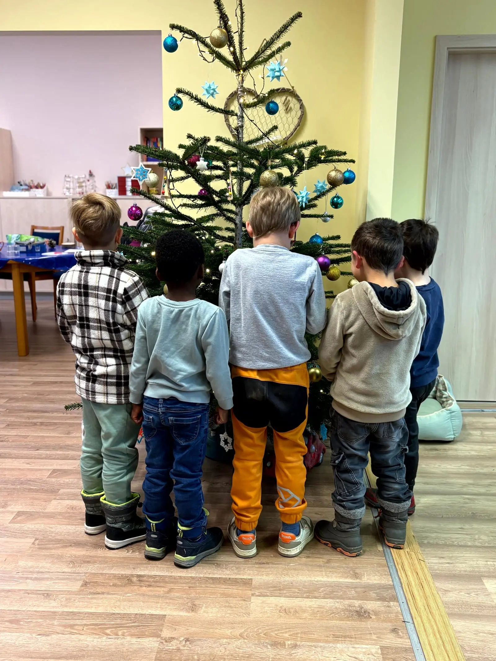 Kinder aus dem Kinderheim stehen vor dem geschmückten Weihnachtsbaum in der Tagespflege