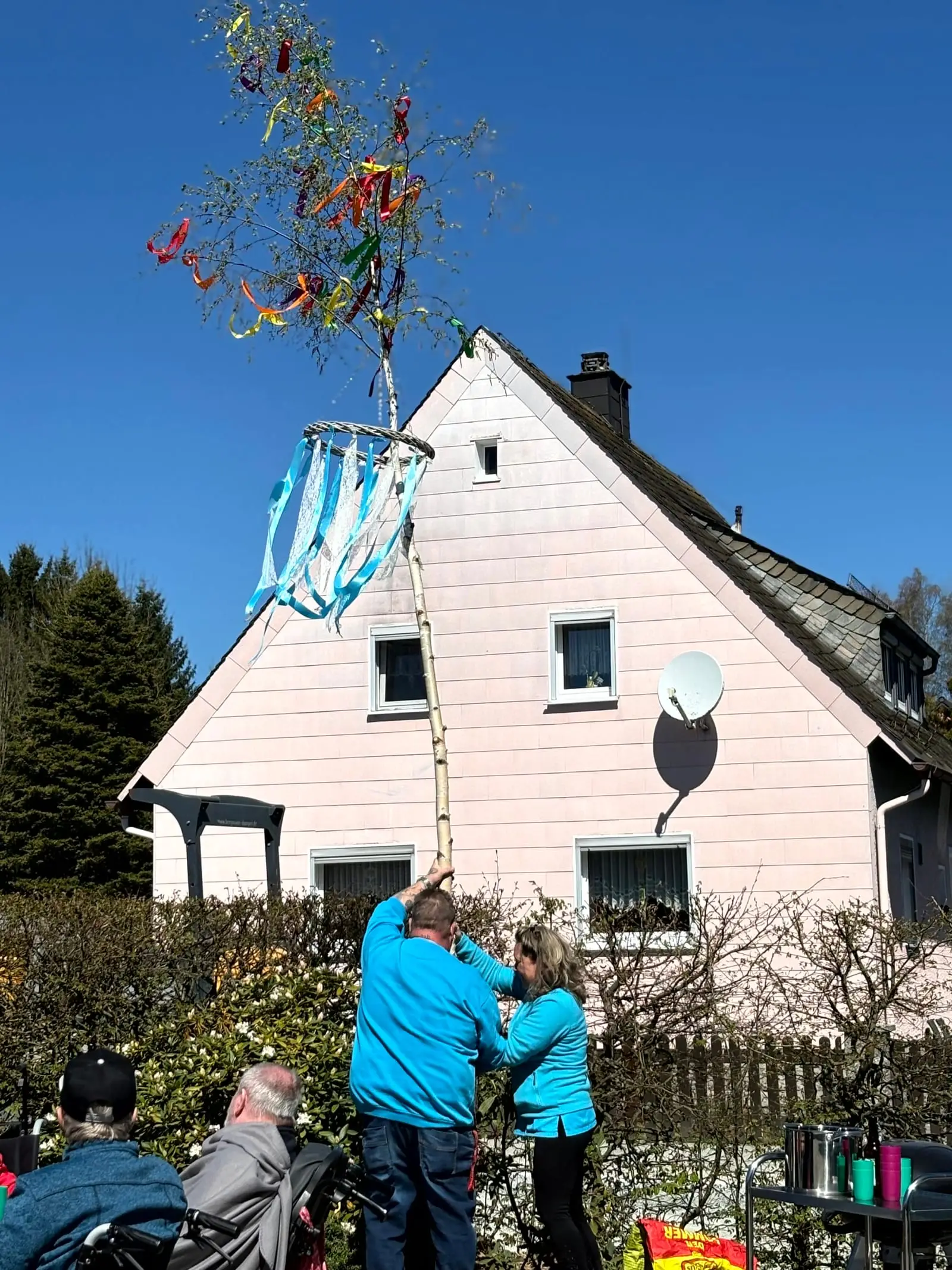 Geschmückter Maibaum mit blau-weißen Bändern vor blauem Himmel