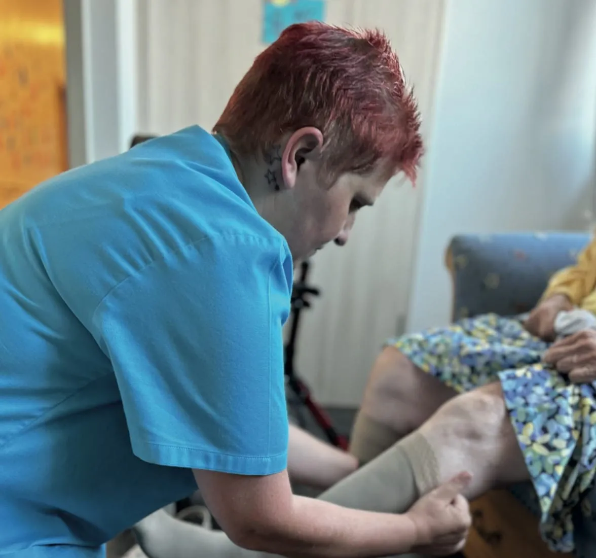 Eine Pflegekraft des ambulanten Dienstes hilft einer Klientin zu Hause beim Anziehen der Kompressionsstrümpfe