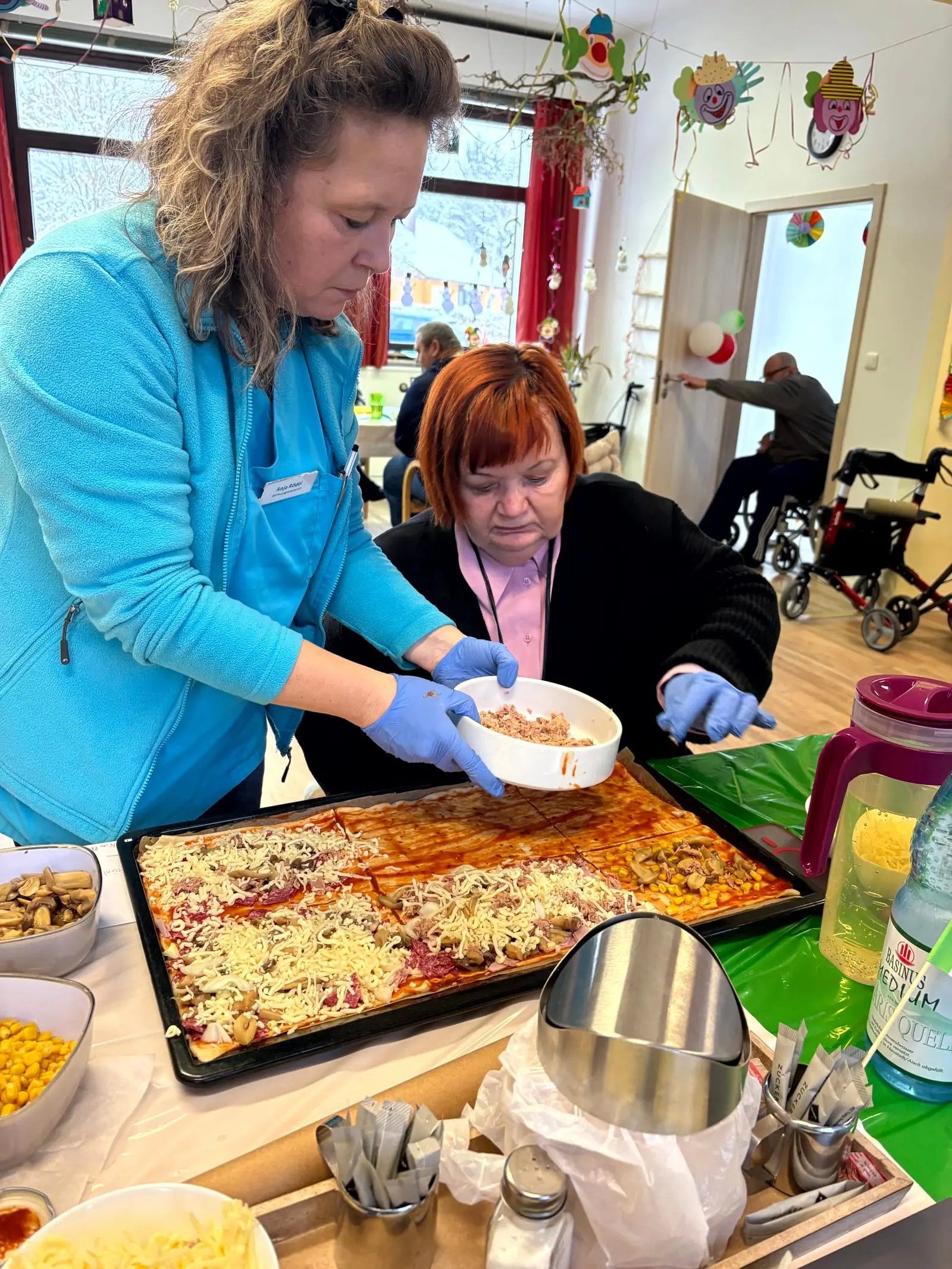 Eine Mitarbeiterin und eine Gästin belegen gemeinsam ein Blech Pizza