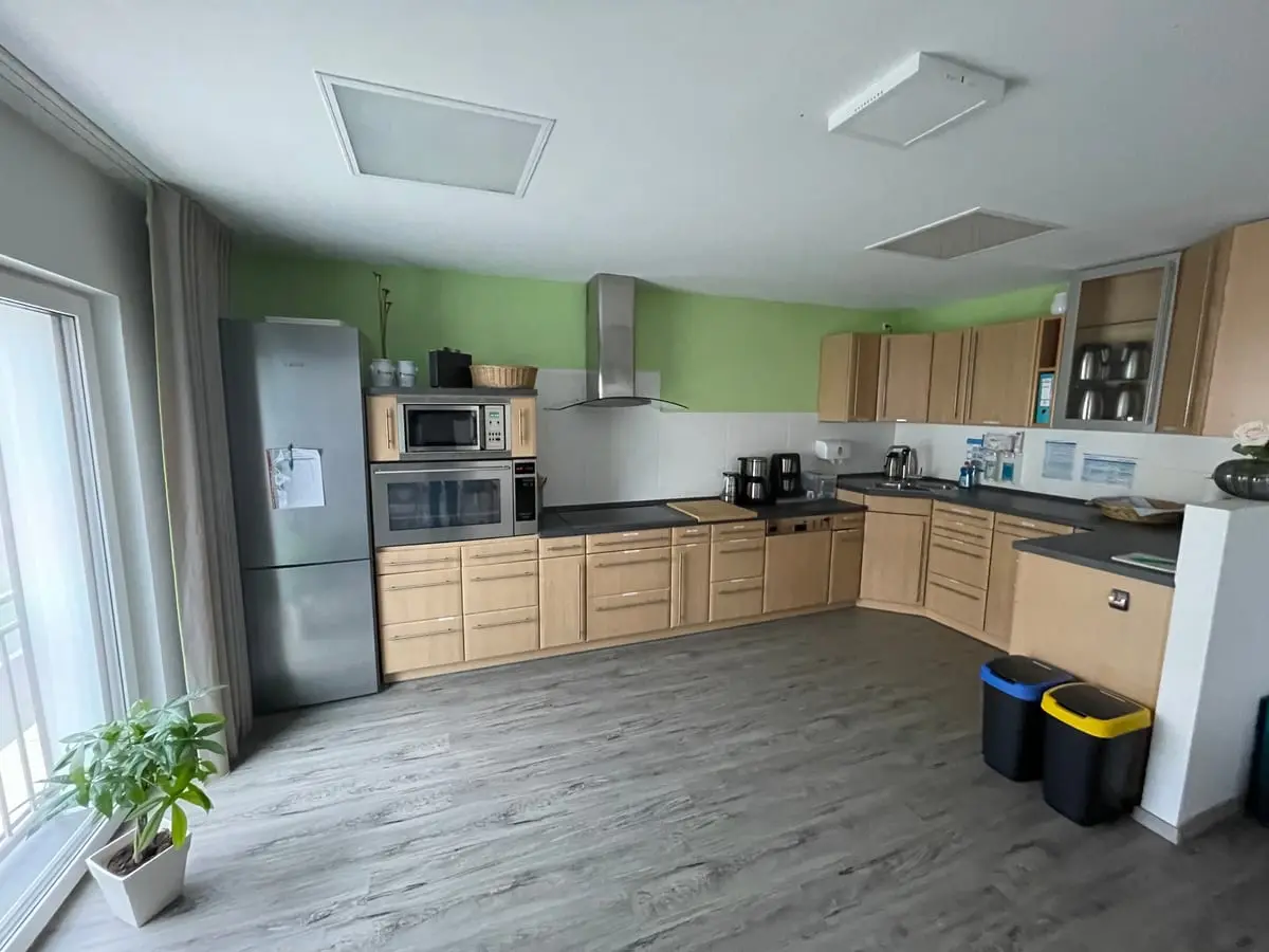 Helle Mitmachküche mit Holzfronten, Kochfeld und großem Kühlschrank