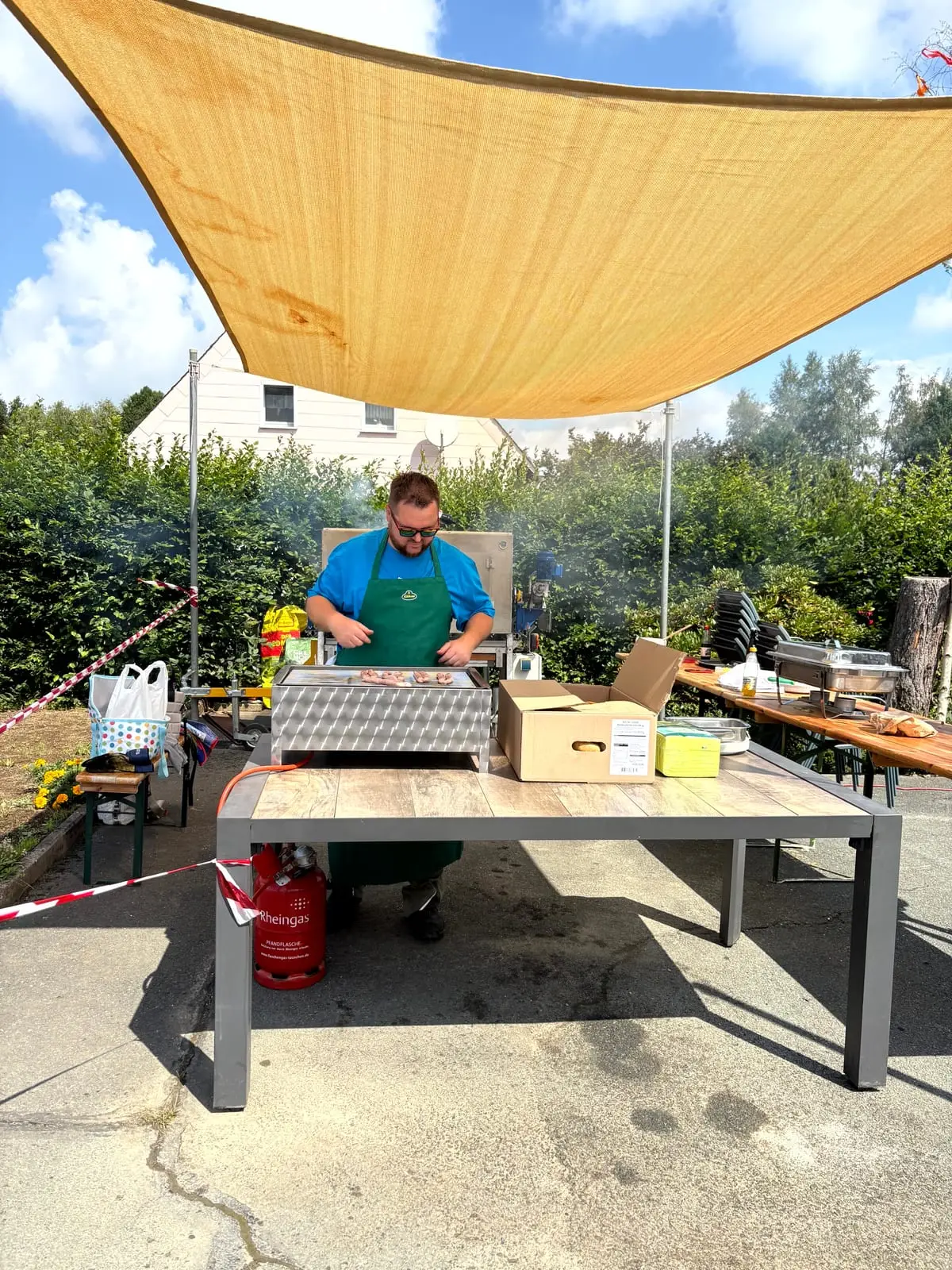 Ein Kollege steht beim Sommerfest am Grill unter dem Sonnensegel